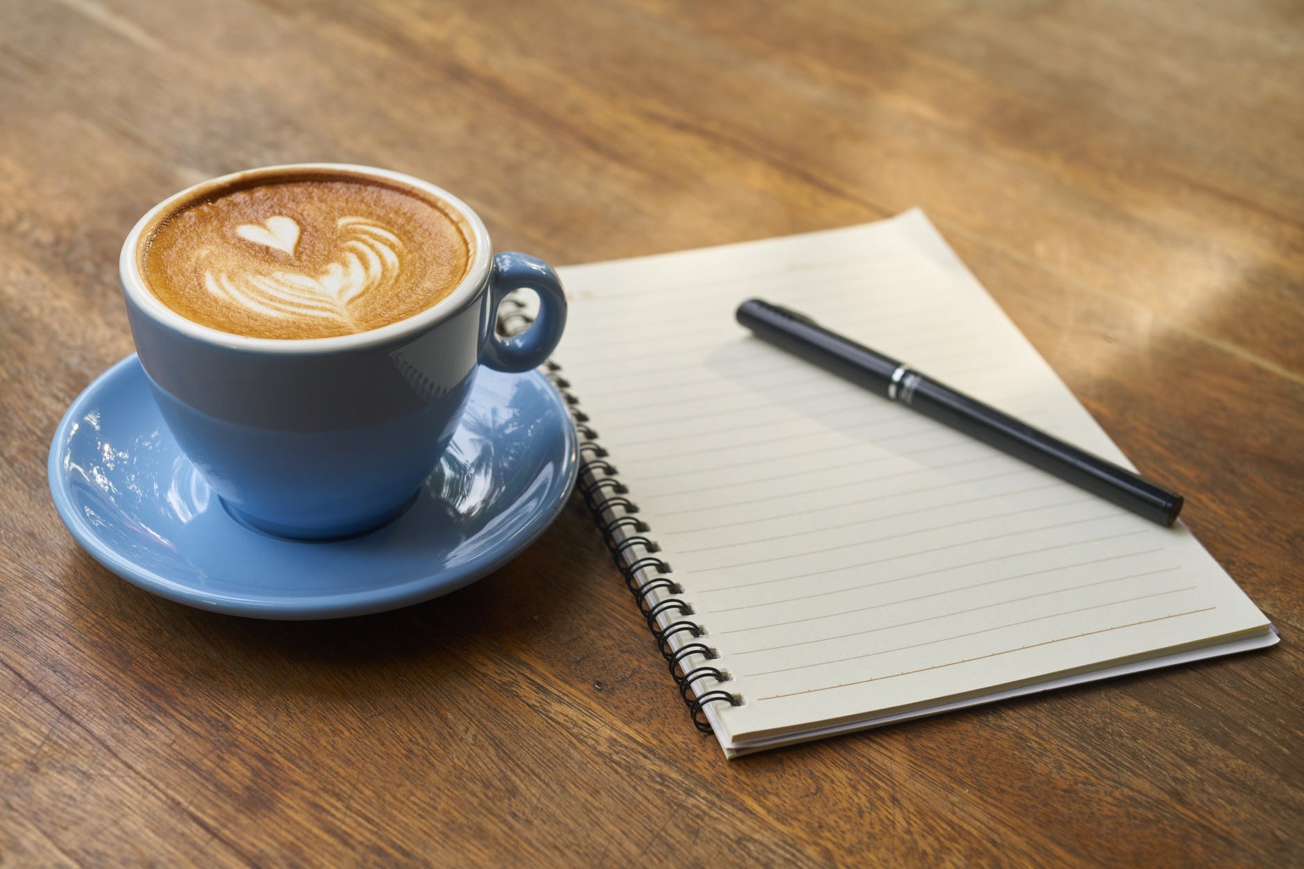 A coffee in a blue cup with a blank notepad and pen ready to start planning a strategy.